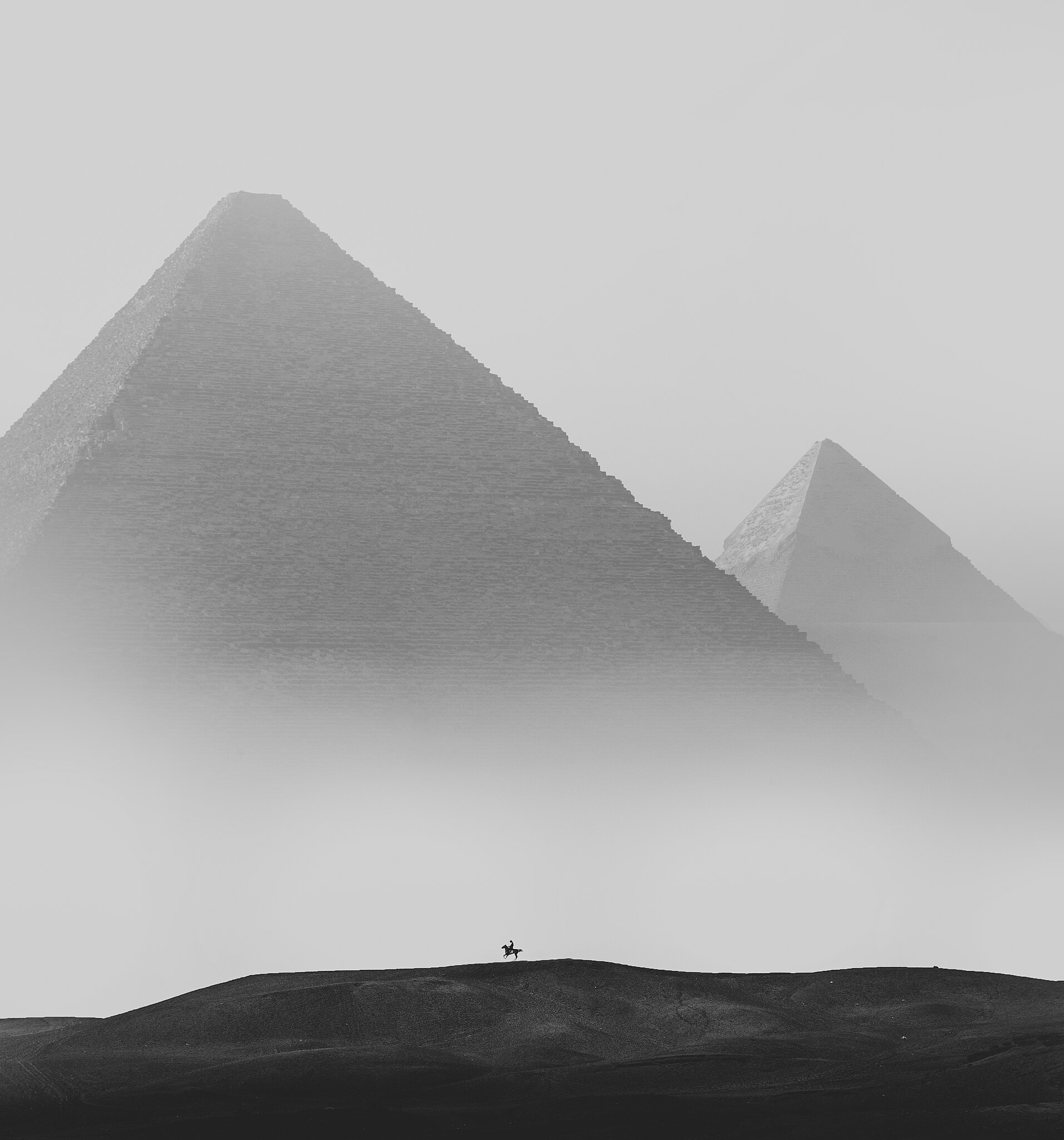 Black and white photography of the Giza Pyramids in Egypt with a horse rider in the foreground
